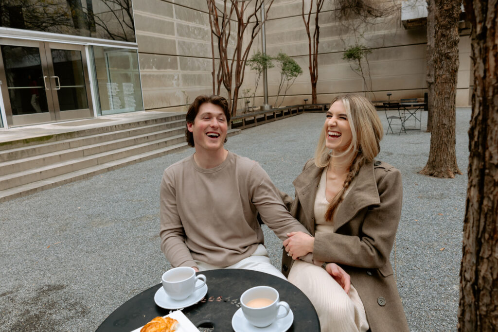 Photograph of an engaged couple sitting down outside of the Dallas museum of Arts laughing together