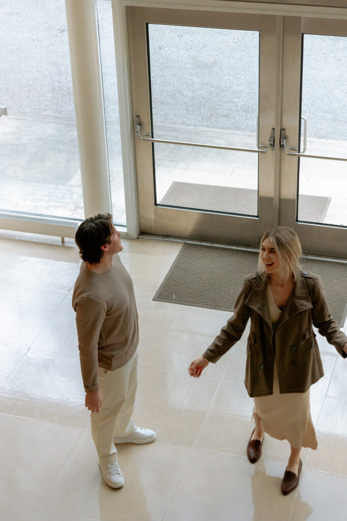 Photograph of an engaged couple laughing together at the Dallas Museum of Arts by the windows