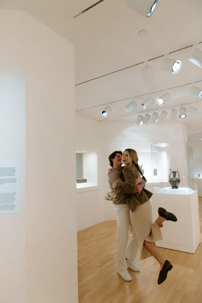 Photo of a man spinning his fiancé around in an art museum while she candidly laughs